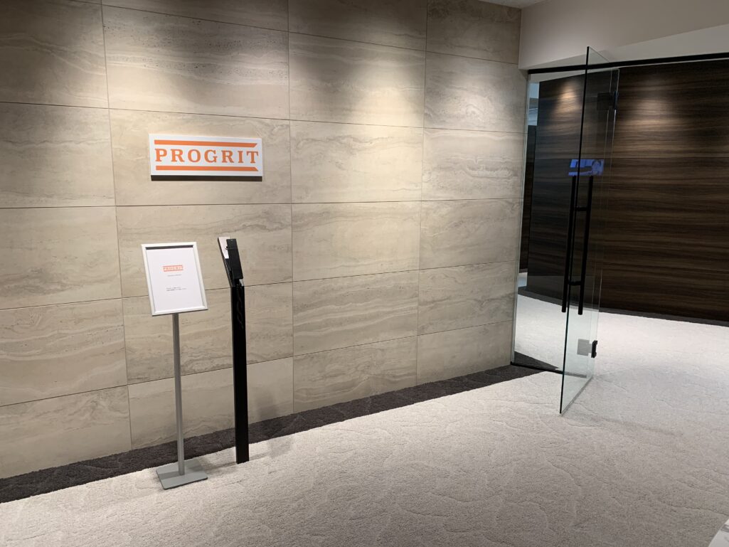プログリット(PROGRIT)の校舎の受付。ロゴの看板と案内スタンド、ガラスの扉