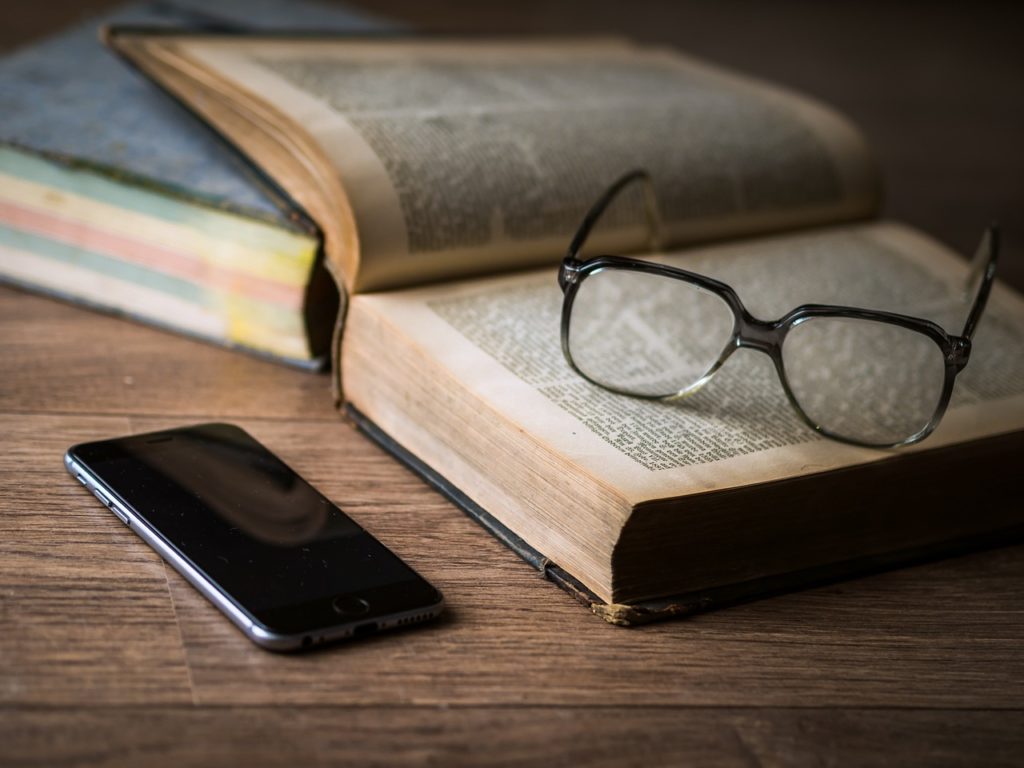 多読の章の写真。木の机に開いた洋書と眼鏡、スマートフォンが置かれている